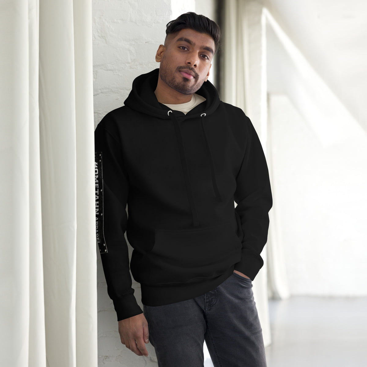 Man wearing a black hoodie leaning against a wall.