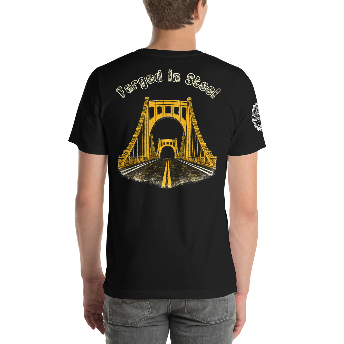 A man wearing a black t-shirt from the back, featuring a yellow graphic of a suspension bridge over a road with the text 'Forged in Steel' above it.
