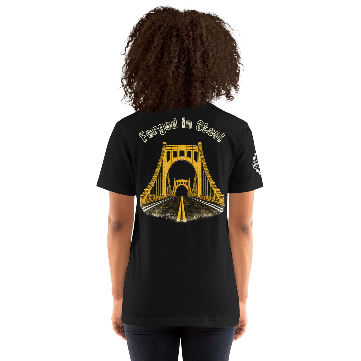 A woman wearing a black t-shirt from the back, featuring a yellow graphic of a suspension bridge over a road with the text 'Forged in Steel' above it.
