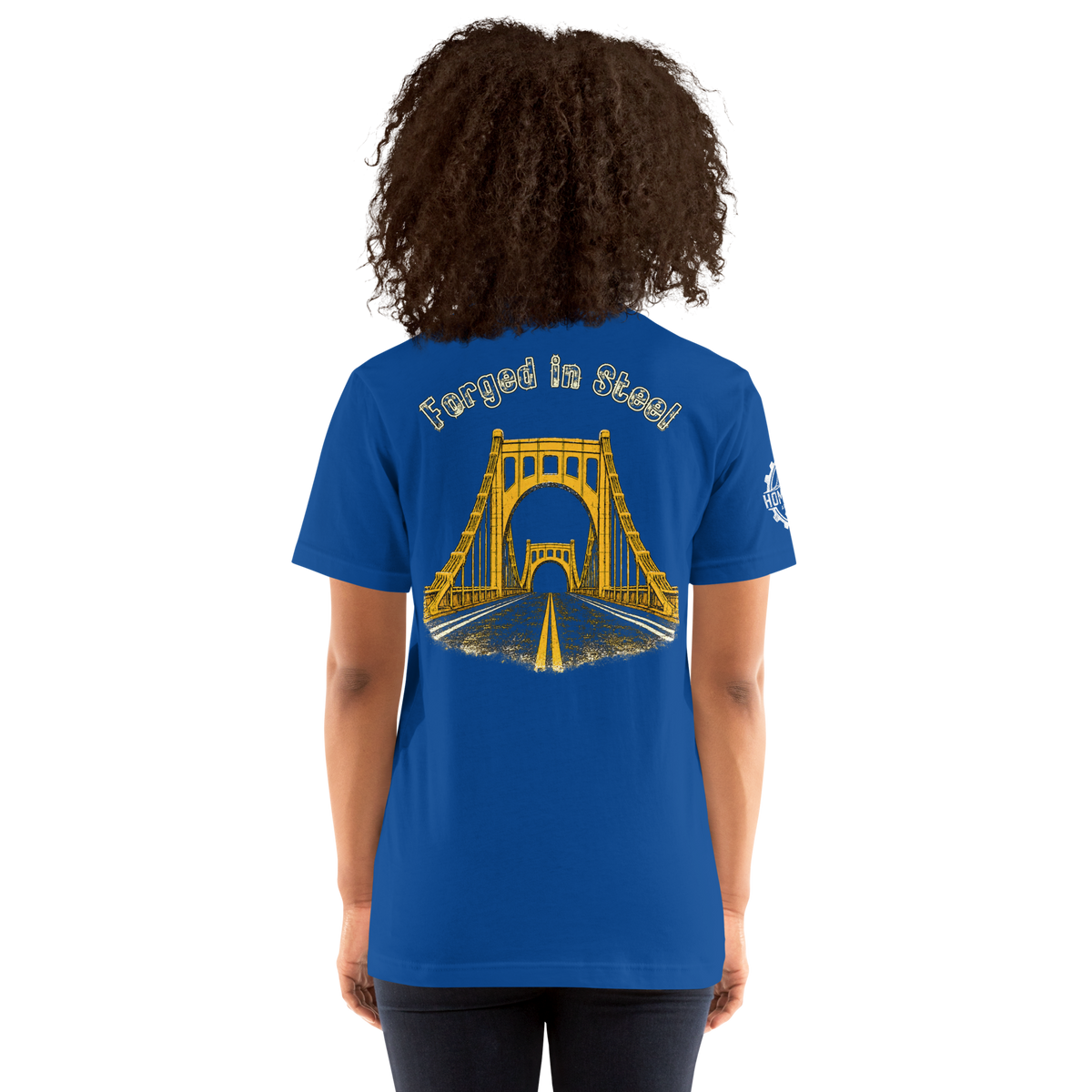 A woman wearing a royal blue t-shirt from the back, featuring a yellow graphic of a suspension bridge over a road with the text 'Forged in Steel' above it.
