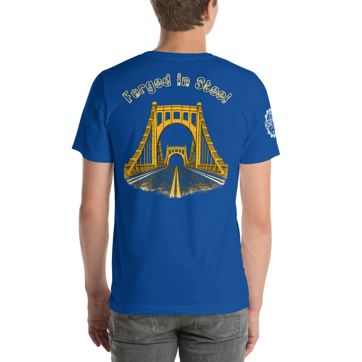 A man wearing a royal blue t-shirt from the back, featuring a yellow graphic of a suspension bridge over a road with the text 'Forged in Steel' above it.
