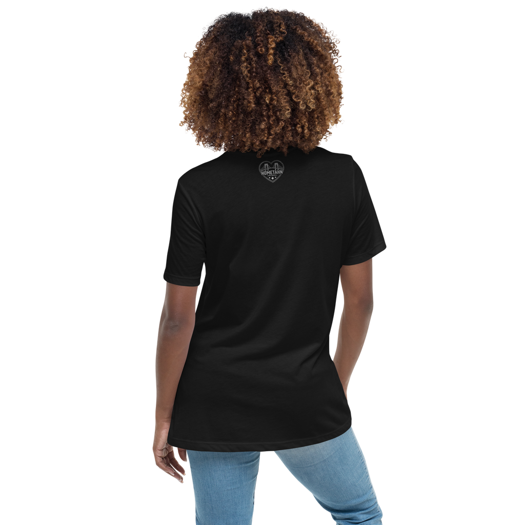 A woman with curly brown hair wearing a black short sleeve t-shirt shown from the back. There is a small heart shaped icon centered at the top, with two bridges and the words "Hometahn Apparel".