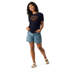 A woman modeling a navy blue t-shirt with a distressed orange and white 'PGH' graphic, paired with denim shorts and white slide sandals, set against a plain white background.