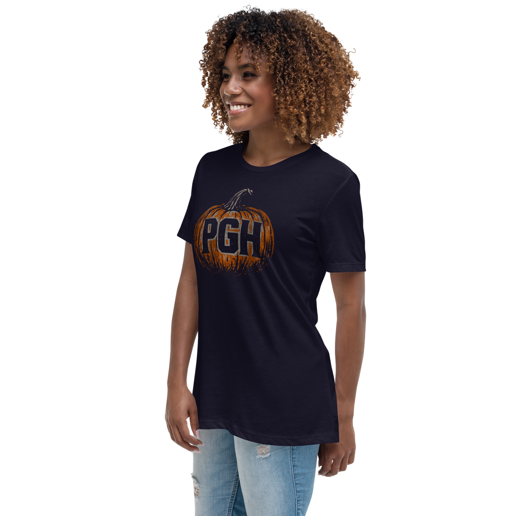 A woman with curly brown hair wearing a navy blue t-shirt with a pumpkin graphic that says 'PGH' in orange and black, paired with light-wash distressed jeans, set against a plain white background.